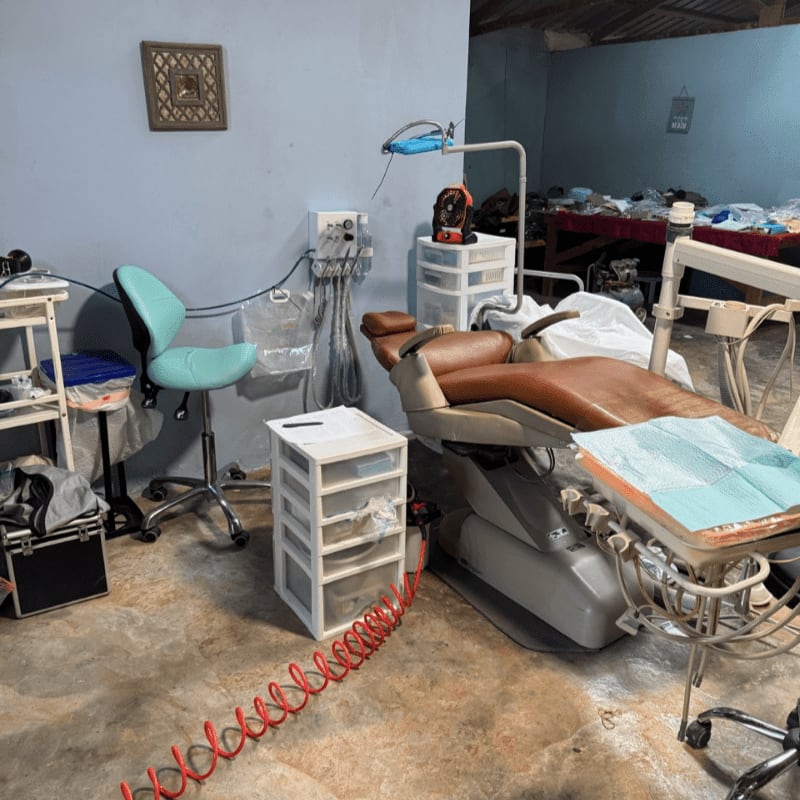 A dental chair and equipment fill the foreground, while a cluttered background reveals shelves and stored items.