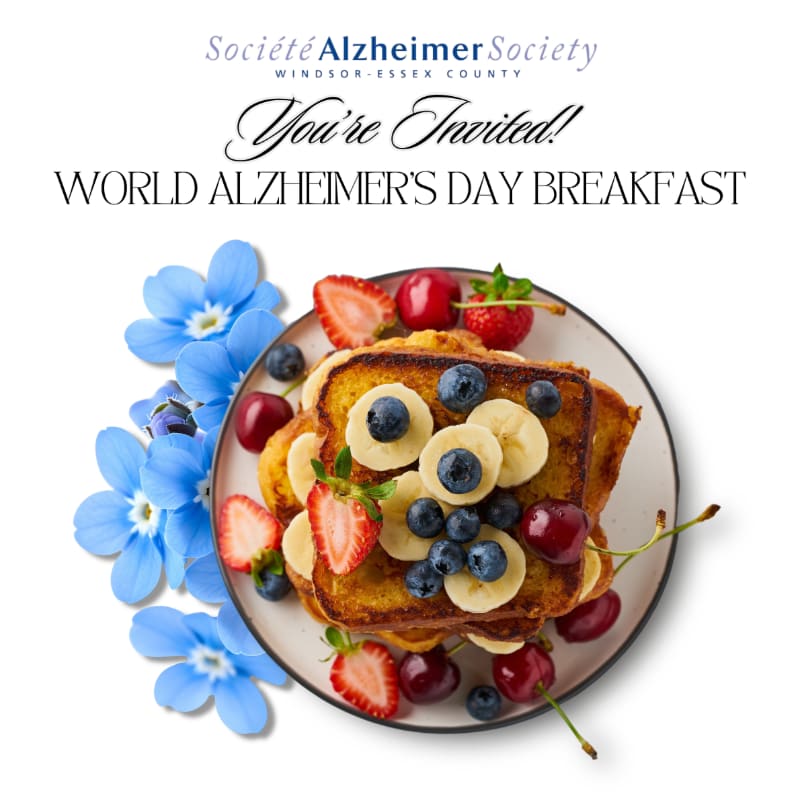 A plate of French toast topped with fruit sits in the foreground, with blue flowers and text announcing a World Alzheimer's Day Breakfast in the background.