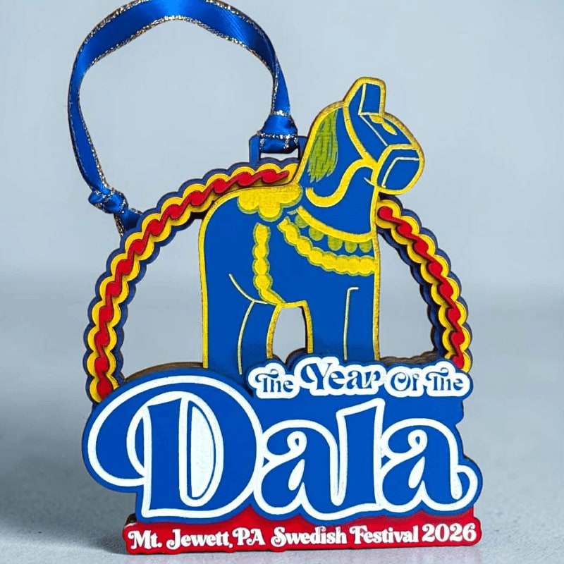 A blue and yellow Dala horse ornament with a red and yellow border hangs against a plain gray background.