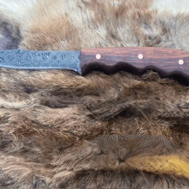 A Damascus steel knife with a wooden handle rests on a bed of brown fur.