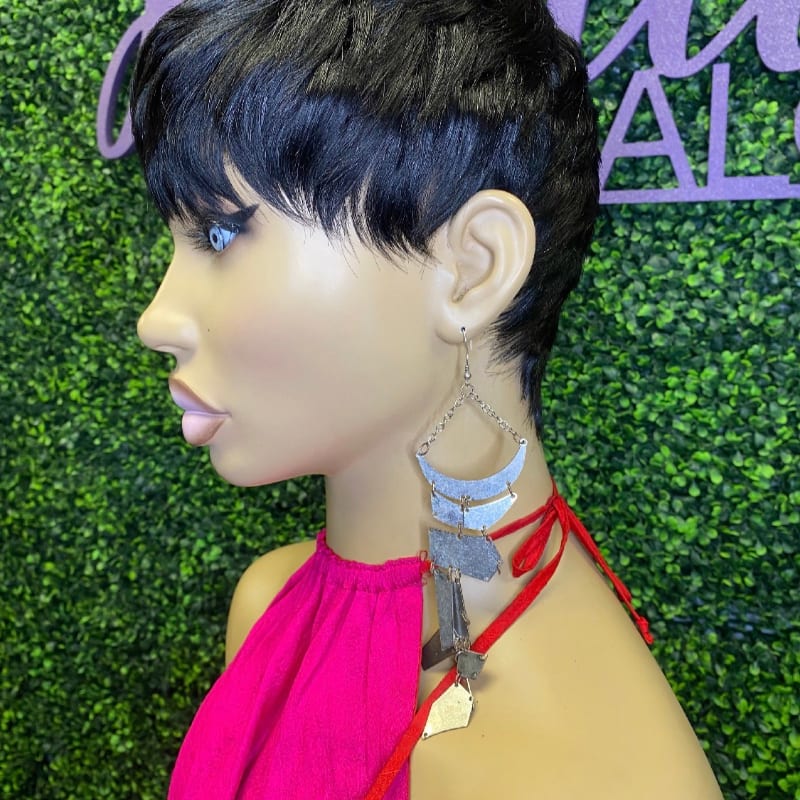 A mannequin with a short black wig and large silver earrings is displayed against a green leafy background.