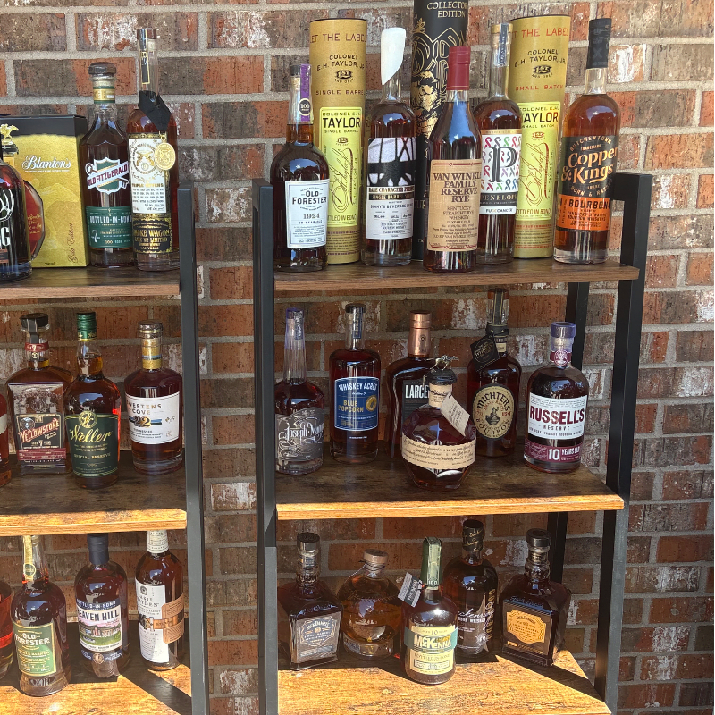 Bottles of whiskey and other spirits are displayed on wooden shelves in front of a brick wall.