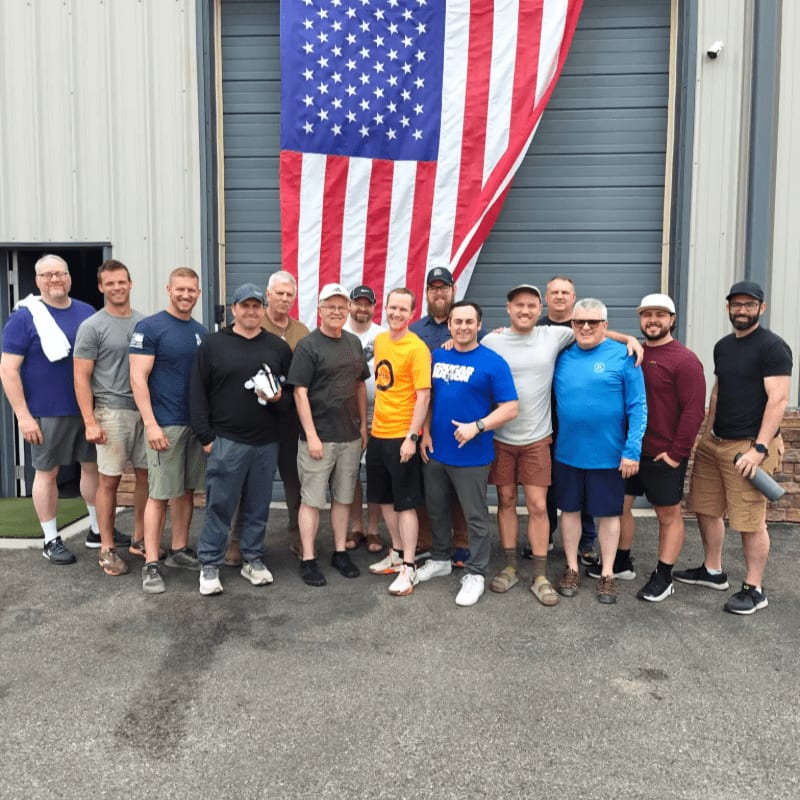 A group of men stand in front of a large American flag displayed on a building.