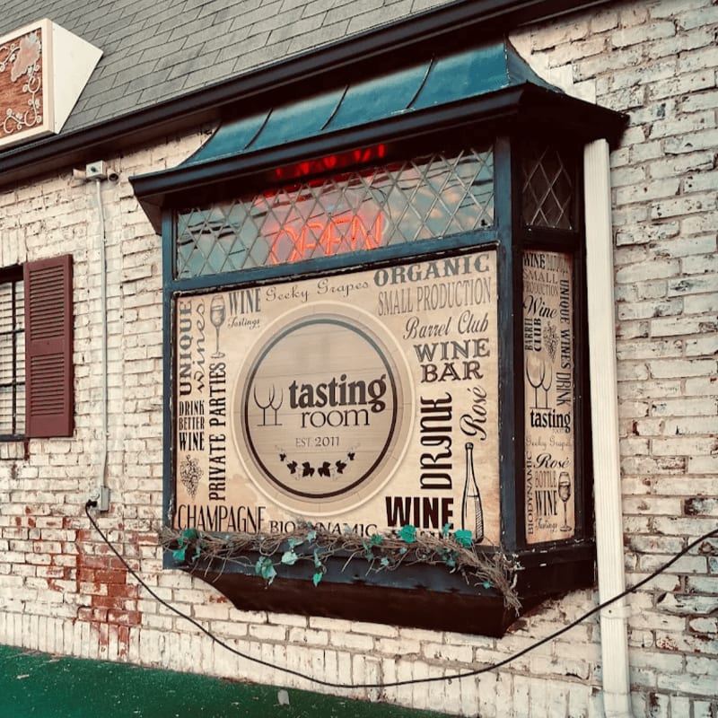 A rustic wine tasting room sign with floral accents is mounted on a white brick building.