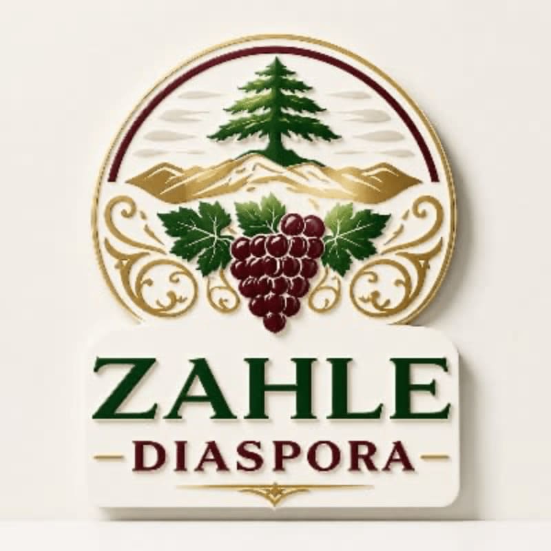 A cluster of dark red grapes and green leaves are in the foreground, set against a circular emblem featuring a cedar tree and mountains, with the words "ZAHLE DIASPORA" below.