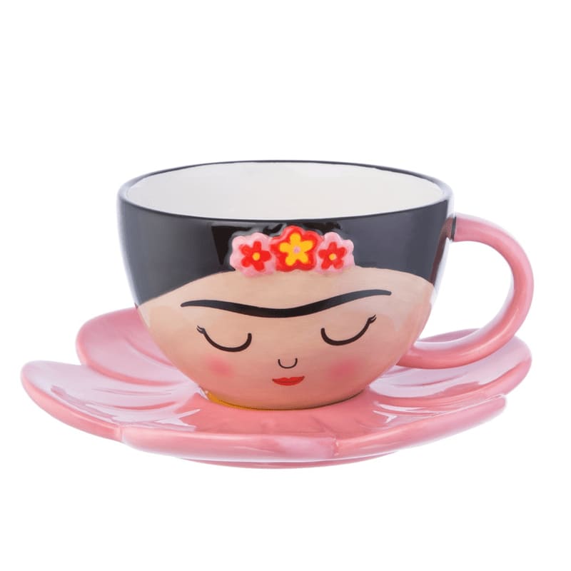A pink, flower-shaped saucer holds a ceramic cup designed to resemble Frida Kahlo's face, set against a plain white background.
