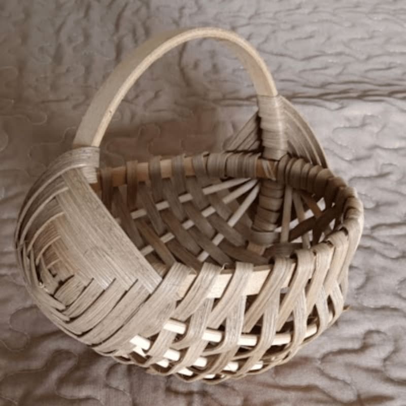 A woven basket with a handle sits on a textured, neutral-colored surface.