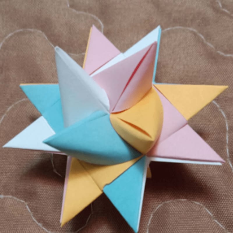 A colorful origami star with pastel points sits on a textured brown fabric background.