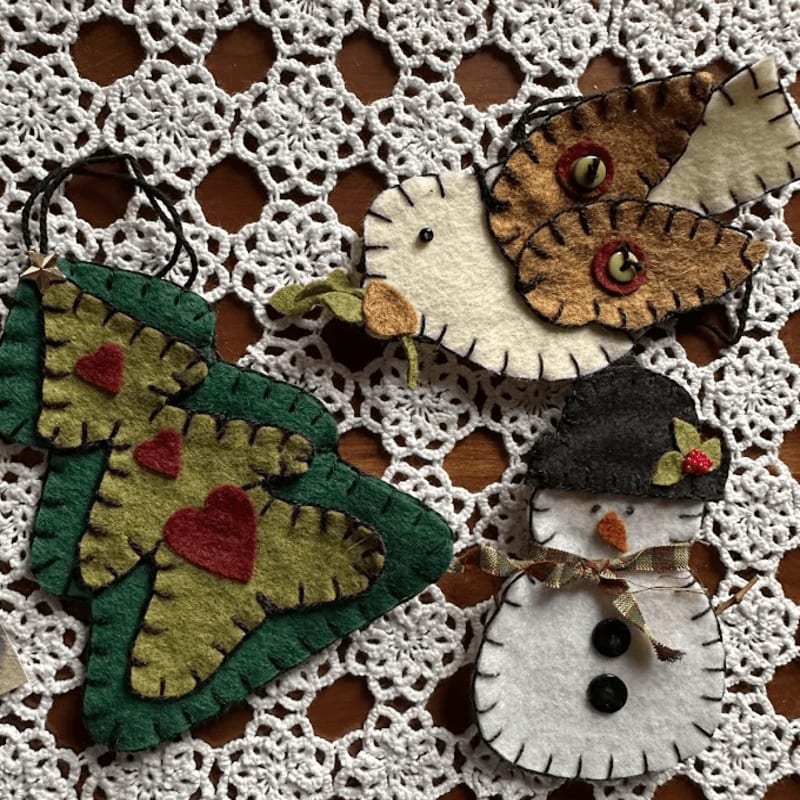 Felt ornaments of a Christmas tree, a butterfly, and a snowman rest on a white crocheted doily.
