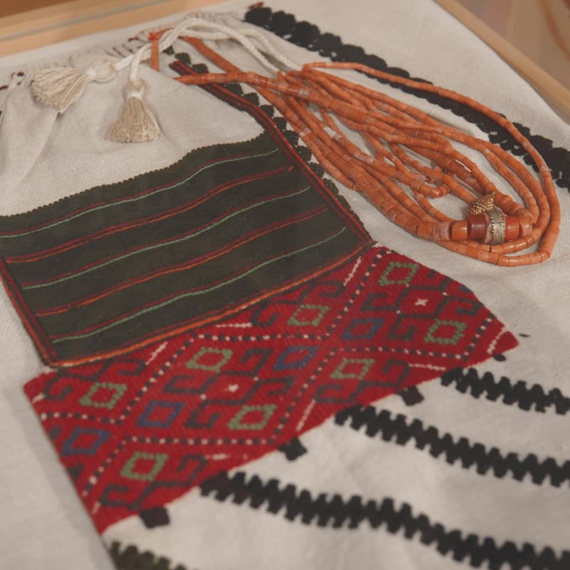A close-up of embroidered fabric with a beaded necklace in the foreground and a blurred background.
