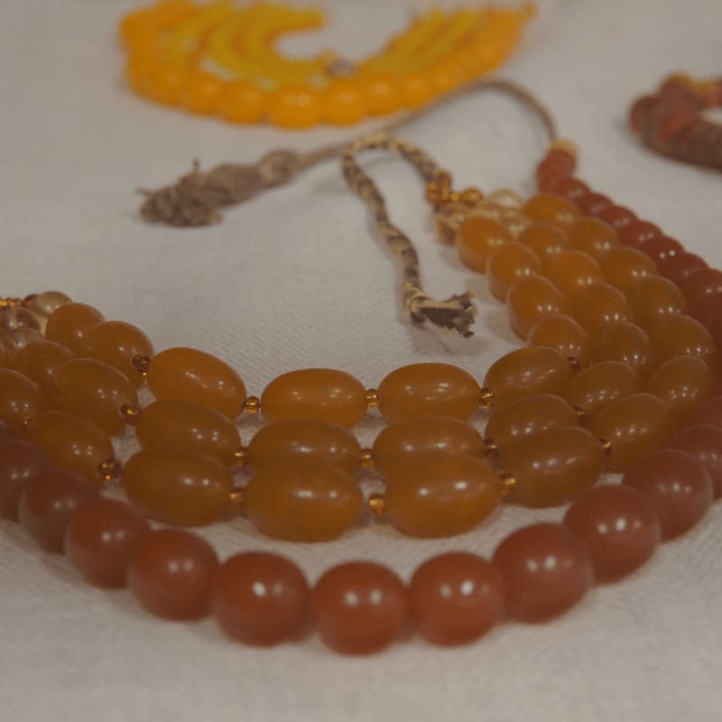 A close-up of amber-colored beaded necklaces in the foreground is set against a blurred background of more jewelry.