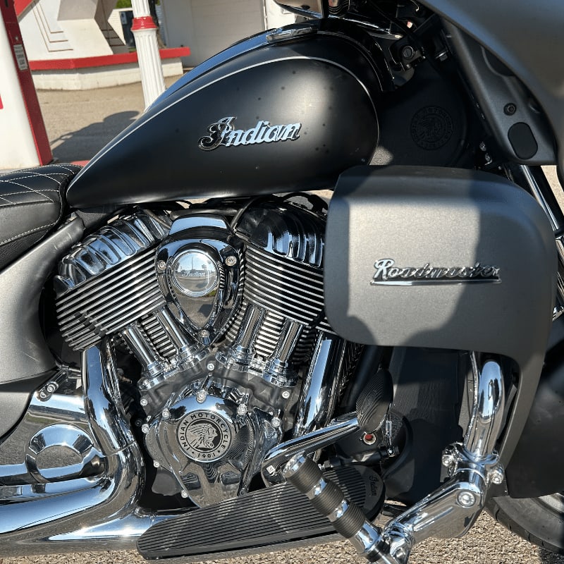 A matte black Indian Roadmaster motorcycle with a chrome engine is parked in front of a red and white structure.