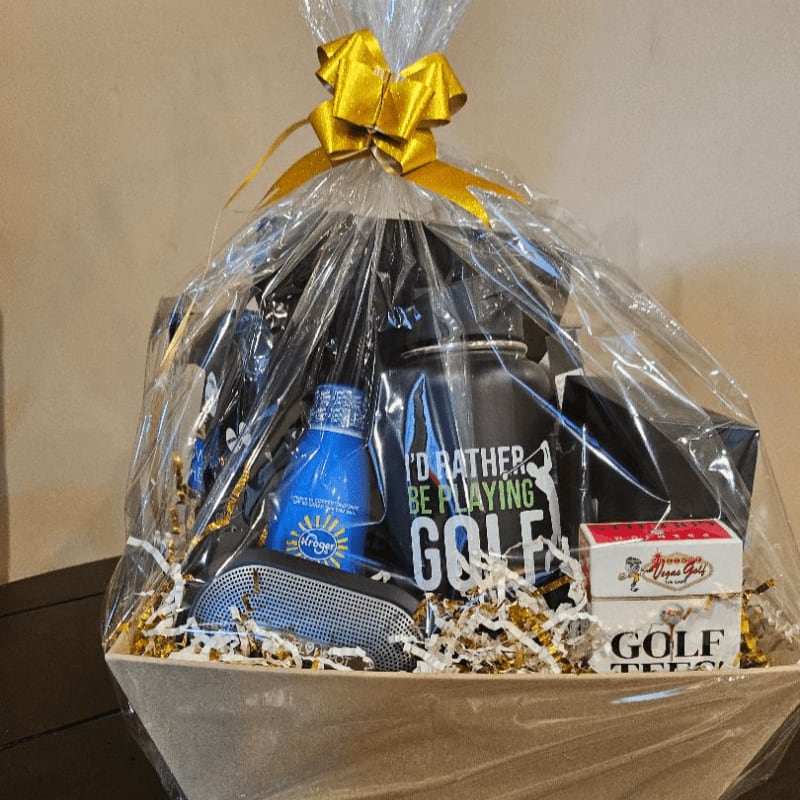 A golf-themed gift basket filled with items like a mug, golf balls, and a speaker is presented in front of a plain, light-colored background.