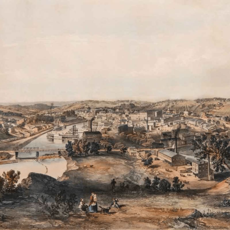 A group of people relax on a grassy hill in the foreground, overlooking a bustling town with a river and factories in the background.
