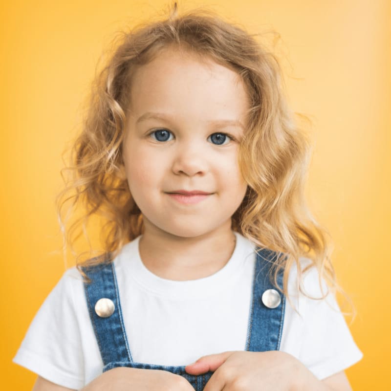 a little girl in overalls posing for a picture