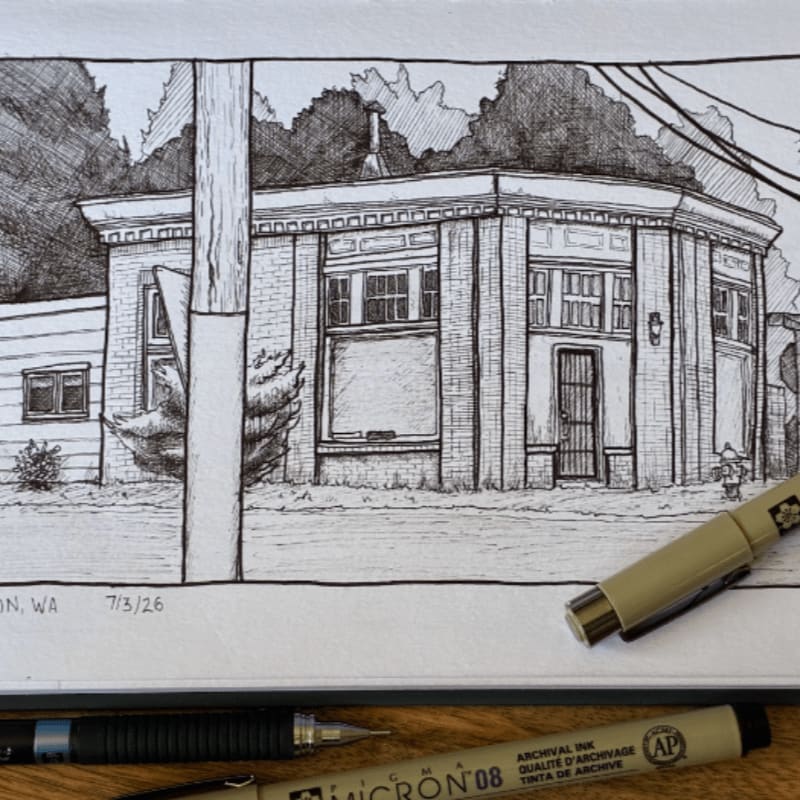 A pen and ink drawing of a brick building with a wooden pole in the foreground is laid out on a surface with drawing pens.