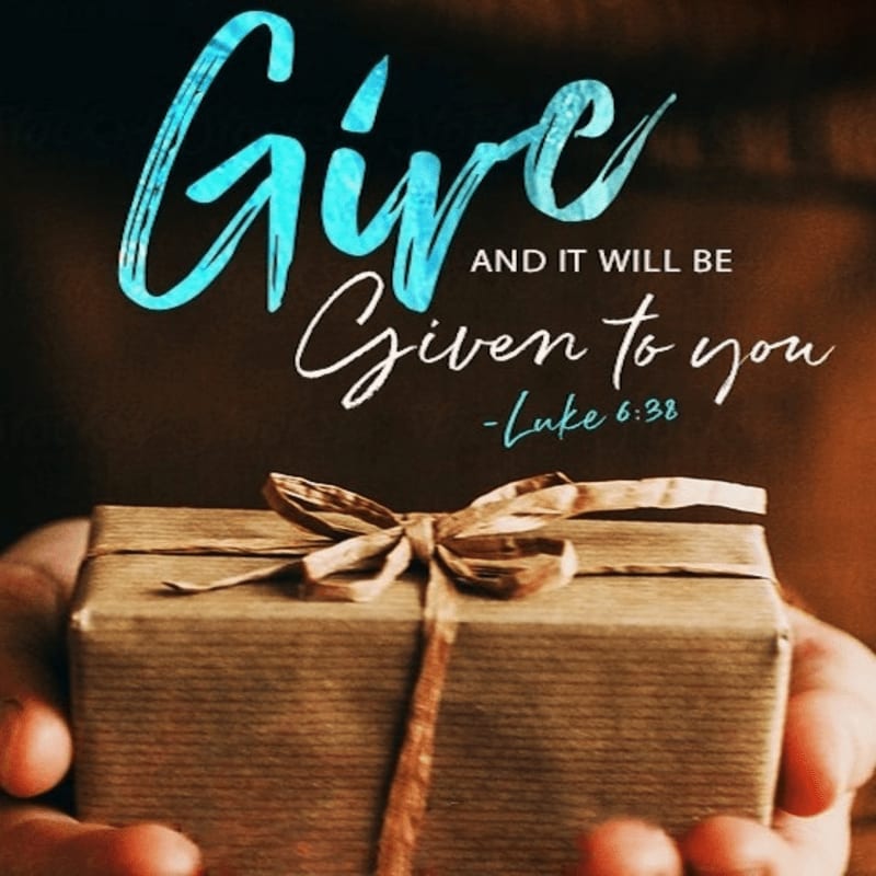 Hands hold a wrapped gift in the foreground, with the words "Give and it will be given to you - Luke 6:38" written in the blurred background.