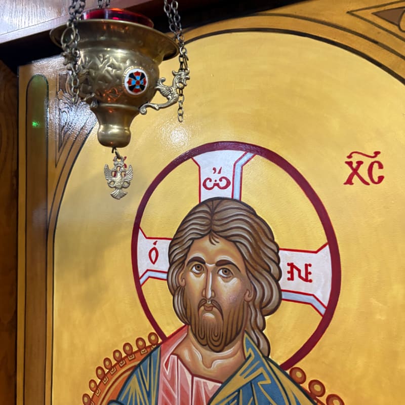 A brass sanctuary lamp hangs in the foreground above a golden icon of Christ with a halo.