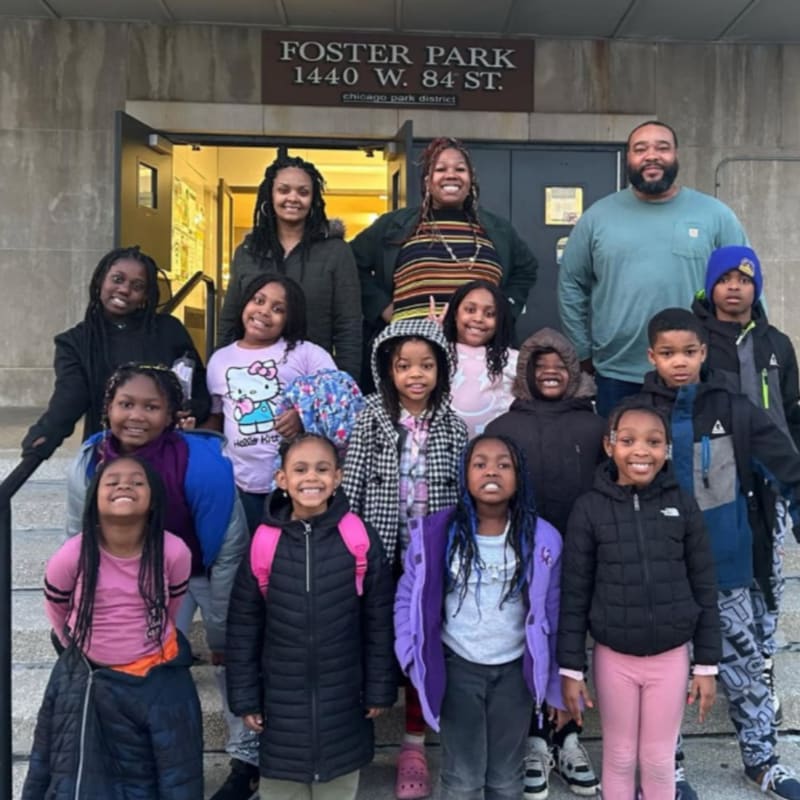A group of children and adults pose for a photo in front of a building with "Foster Park" signage.