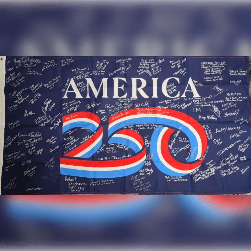 A dark blue flag with "AMERICA 250" emblazoned in white and red, white, and blue ribbon-like lettering is covered in numerous handwritten signatures.