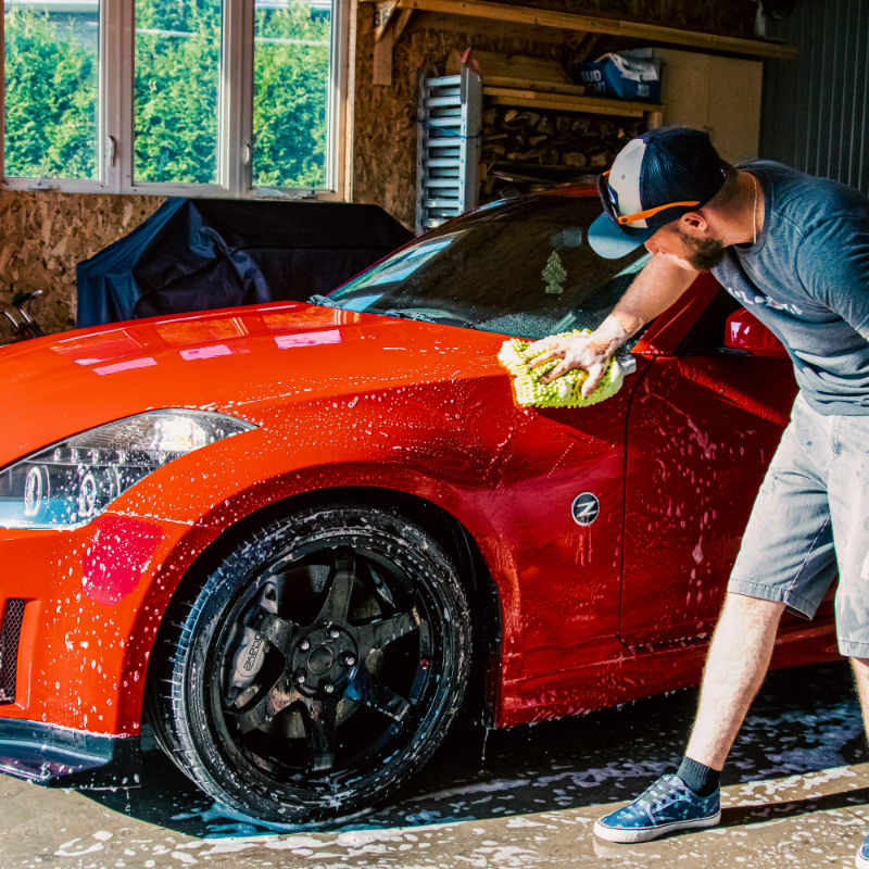 a man washing a red sports car in a garage