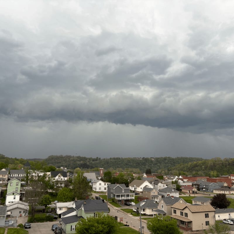 A small town with houses and trees sits under a dark, stormy sky.