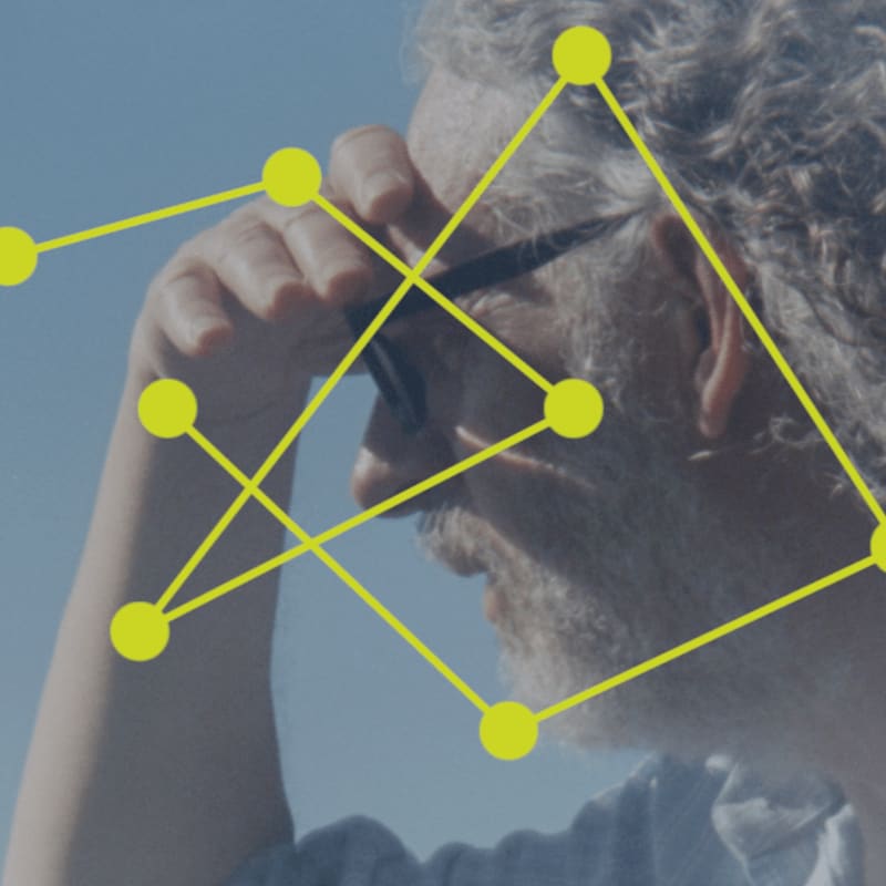 A man with graying hair and glasses shields his eyes from the sun, with a yellow geometric pattern overlaid on the clear blue sky.