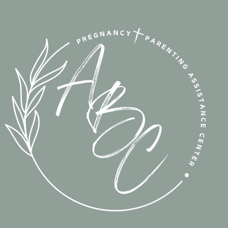 A white logo with the letters "ABC" in a cursive font is centered on a muted green background, encircled by a laurel branch on the left and text reading "PREGNANCY + PARENTING ASSISTANCE CENTER" on the right.