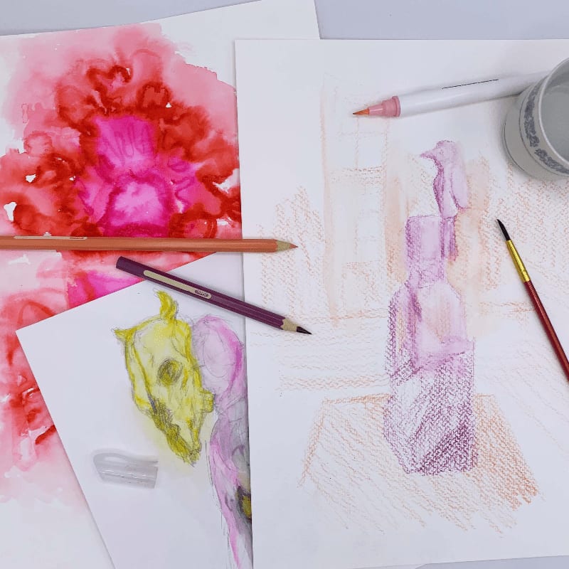 Art supplies, including colored pencils, markers, and brushes, are scattered across sketches of abstract flowers and a still life of bottles.