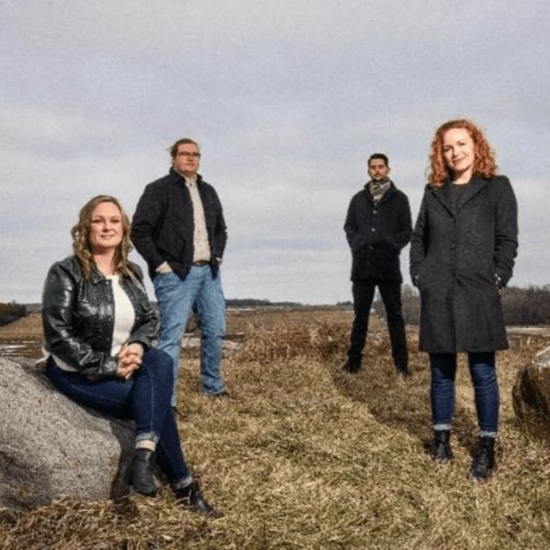 Four people stand in a grassy field with a cloudy sky above.