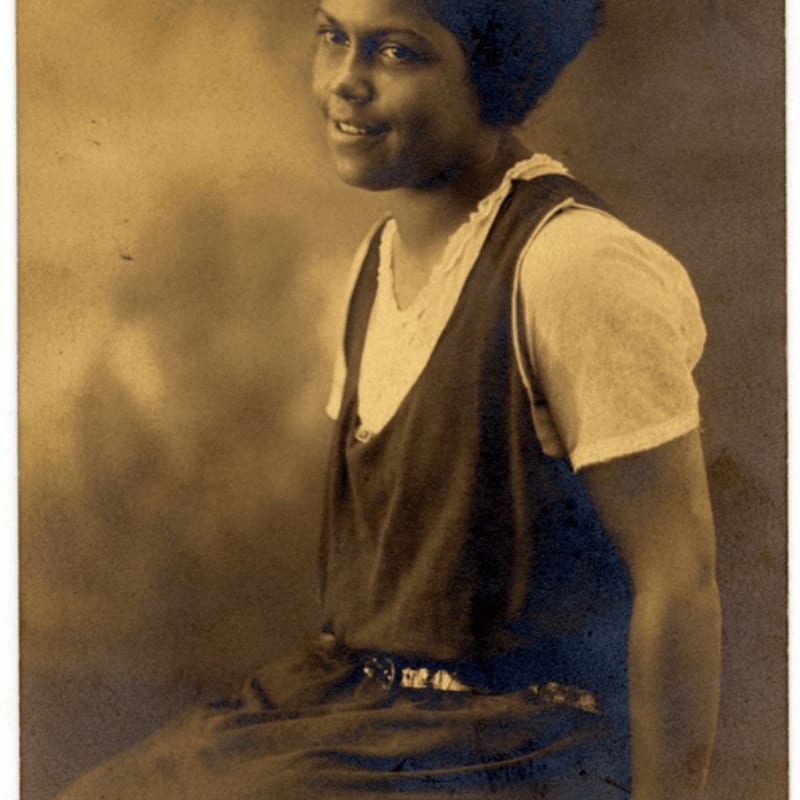 A young woman in a dark dress and white blouse smiles softly against a mottled, sepia-toned background.