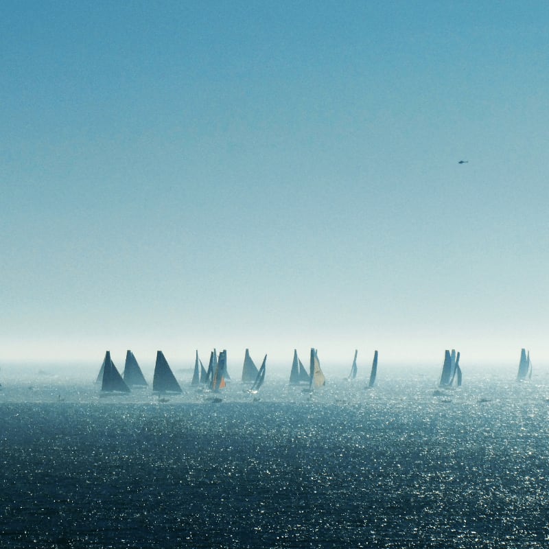 a group of sailboats sailing in the ocean on a foggy day