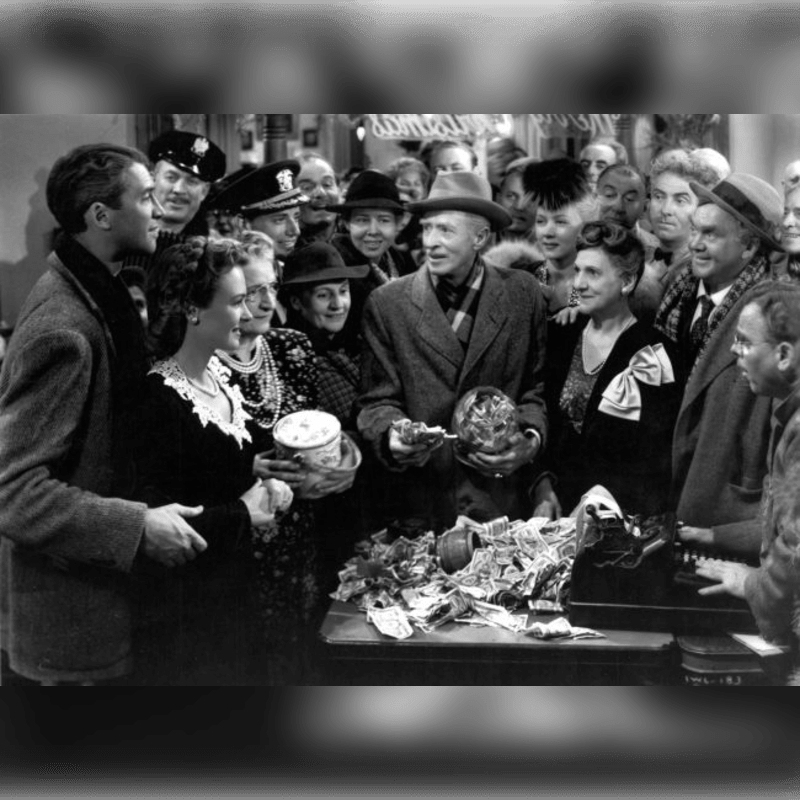 A crowd of people, some in uniform, gather around a table laden with money and gifts, with a man in a hat holding a glass orb.
