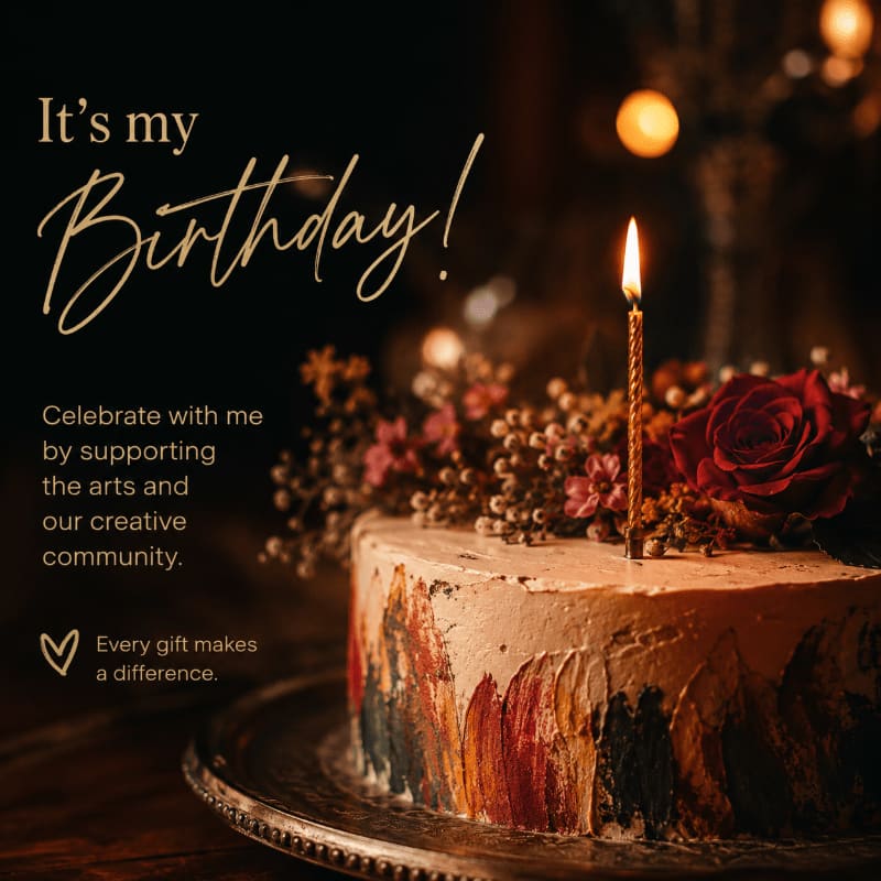 A festive birthday cake with a single lit candle sits on a platter in the foreground, while a softly blurred background features warm, glowing lights and floral decorations.