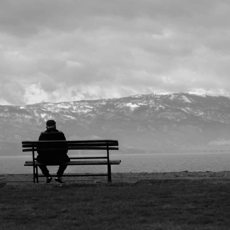 grayscale photo of man sitting on bench