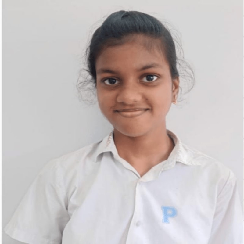 A young girl with dark hair pulled back smiles at the camera in a white collared shirt against a plain gray background.