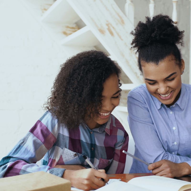 Two women smiling while studying at a table.