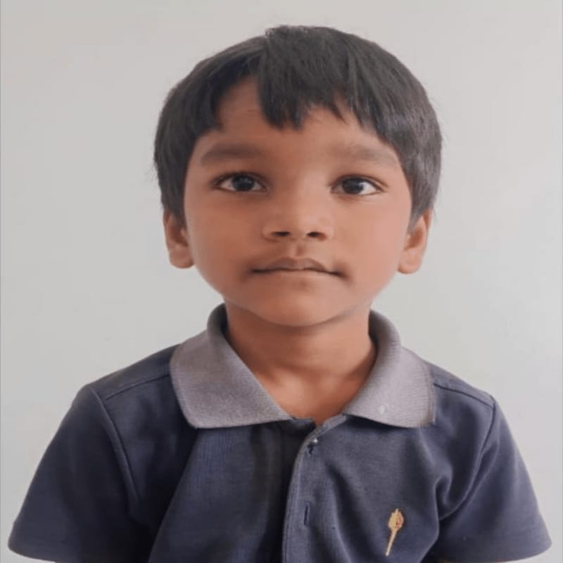 A young boy with dark hair and a serious expression wears a dark blue polo shirt in the foreground, set against a plain, light gray background.
