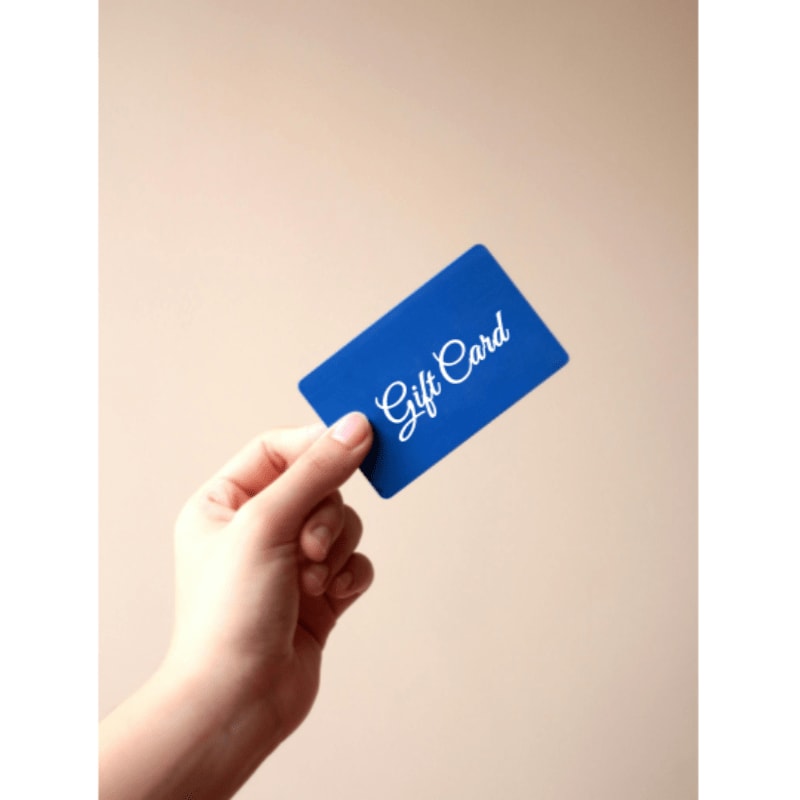A hand holds a blue gift card against a plain, light-colored background.
