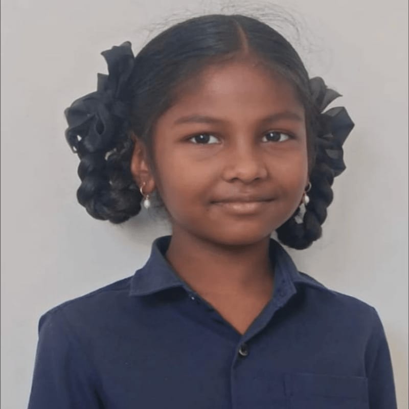 A young girl with dark hair in pigtails smiles gently against a plain, light-colored background.