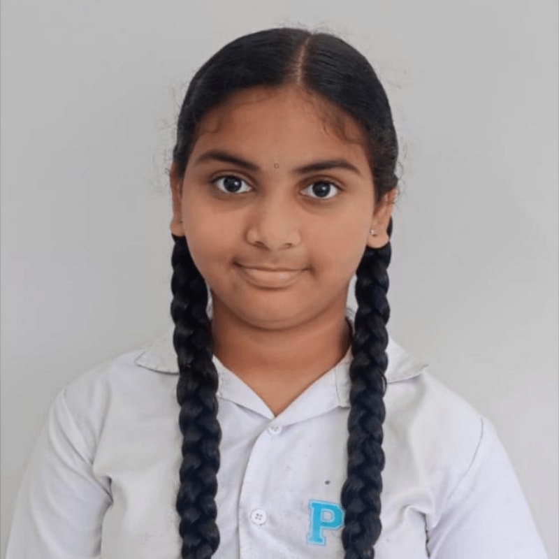 A young girl with braided hair and a white collared shirt stands against a plain, light gray background.