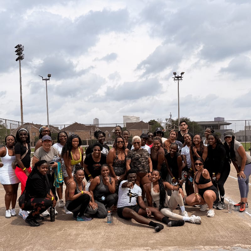 A group of people pose for a photo on a tennis court with buildings and a cloudy sky in the background.