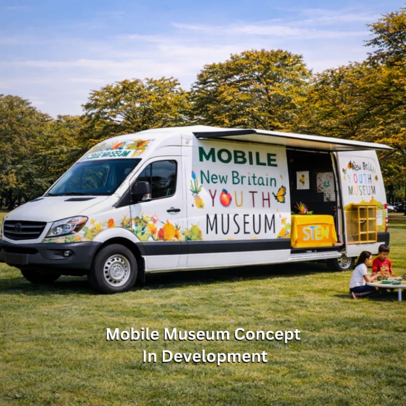A white mobile museum van with colorful graphics is parked on a grassy field with two children engaged in an activity in the foreground, set against a backdrop of trees and a blue sky.
