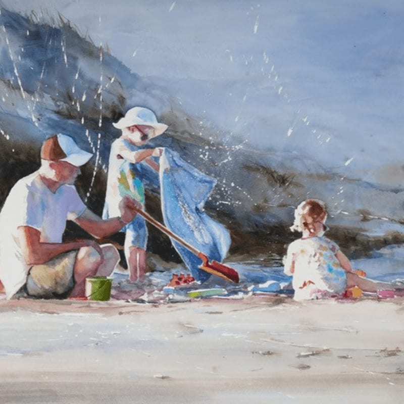 A man and two children play on a sandy beach with a rocky cliff in the background.
