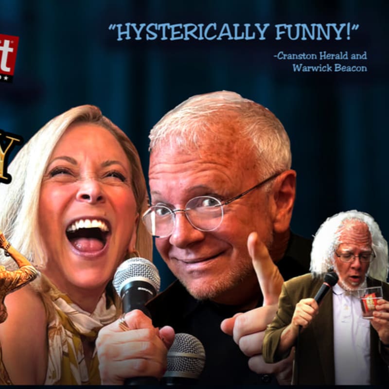 A woman with blonde hair laughs heartily into a microphone in the foreground, while a man with glasses and a man with white hair and a beard are visible in the background.