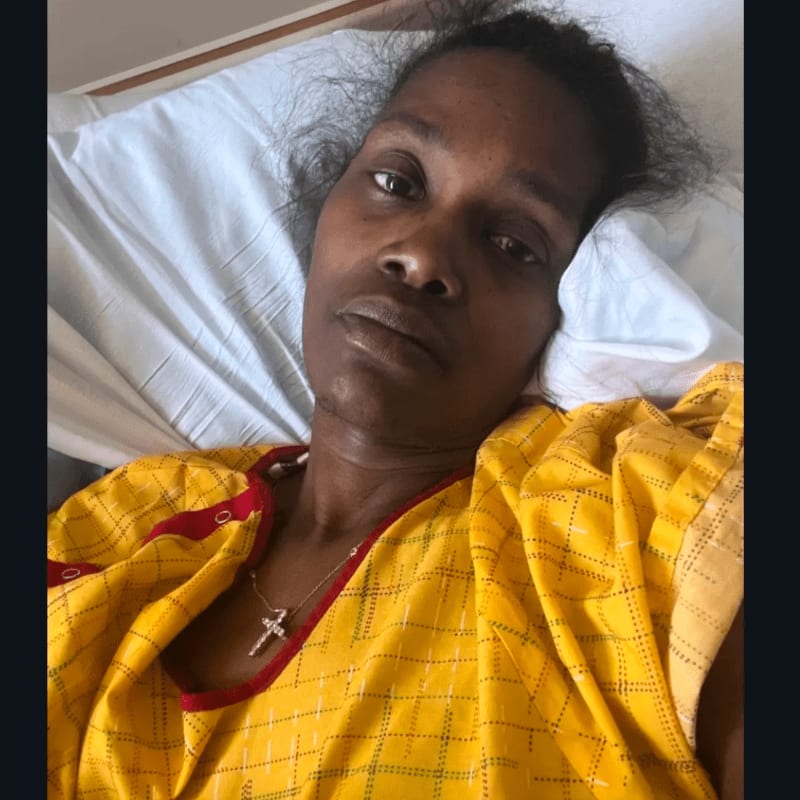 A woman in a yellow hospital gown rests on a white pillow in a hospital bed.