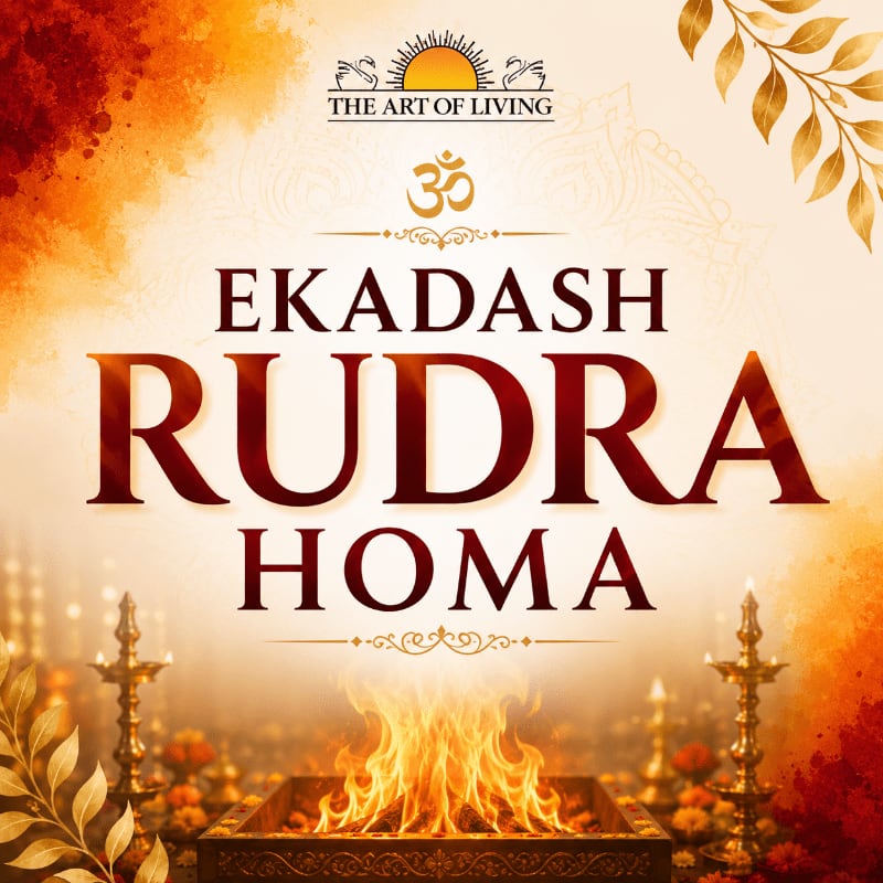 A vibrant Homa fire burns in the foreground, set against a warm, ornate background featuring the "The Art of Living" logo and decorative elements.