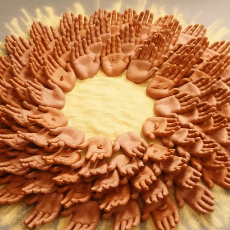 A circular arrangement of clay hands with open palms forms the foreground, set against a textured yellow background.