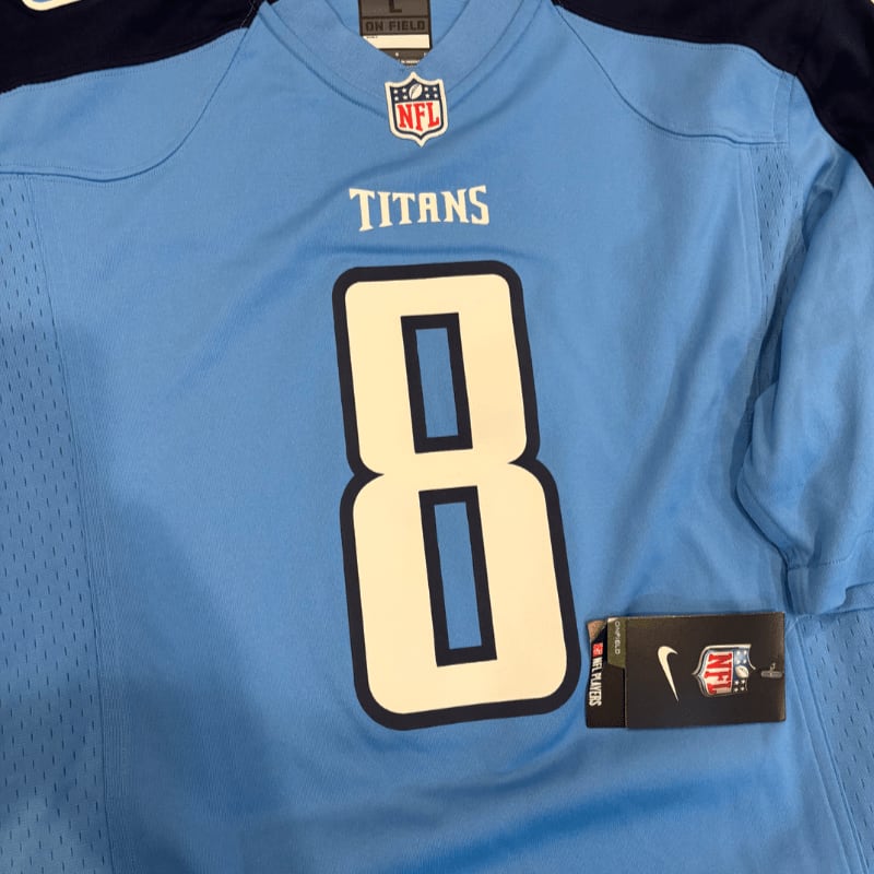 A light blue Tennessee Titans jersey with the number 8 prominently displayed in the foreground, rests against a dark blue background.