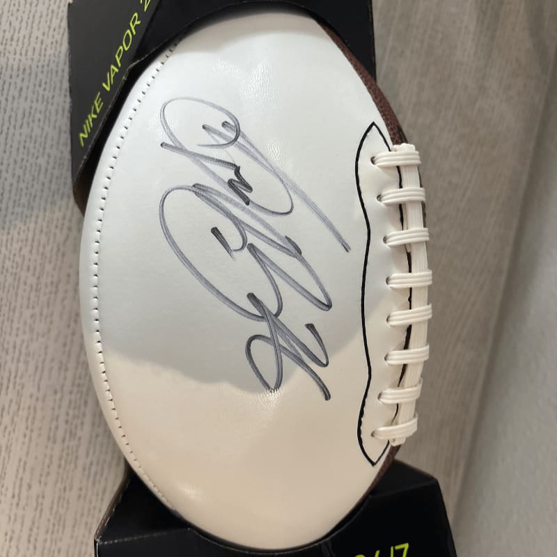 A white football with a black signature rests on a black box with a white Nike logo in the background.